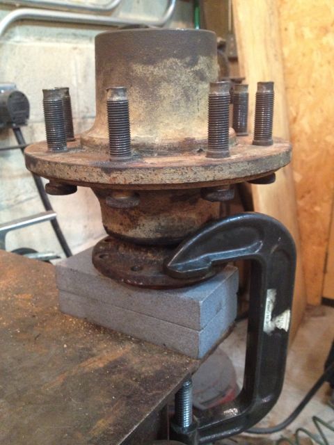 1989 Ford Bronco - A close-up view of a rusty wheel hub assembly secured with a C-clamp and resting on blocks.