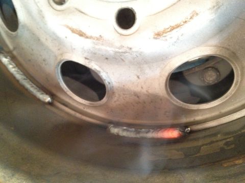 1989 Ford Bronco - Welding is being performed on a metal wheel rim, indicated by the glowing metal and visible weld beads.
