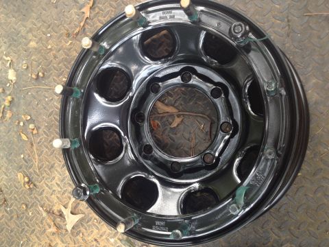 1989 Ford Bronco - A black steel wheel with chrome lug nuts and green plastic inserts on studs is shown.