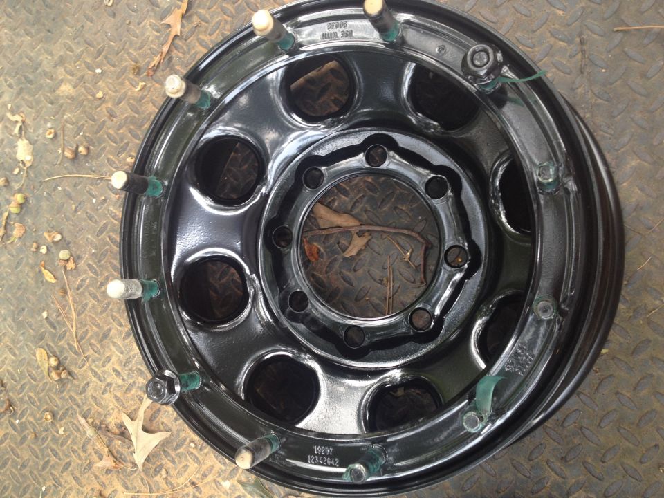 Black steel wheel with chrome lug nuts and green plastic inserts on studs