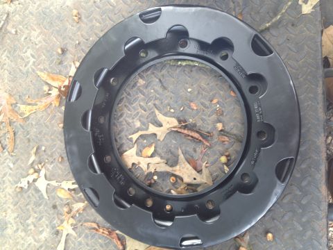 1989 Ford Bronco - A black wheel rim with distinctive cutouts is shown resting on a diamond plate surface with fallen leaves.