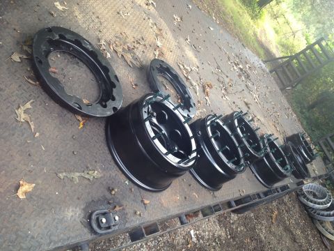 1989 Ford Bronco - Black rims and beadlock rings are laid out on a trailer, ready for installation.