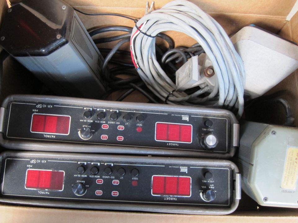 Two KR 10 SP radar detector units with red displays and controls, plus other electronic components and cables in a box