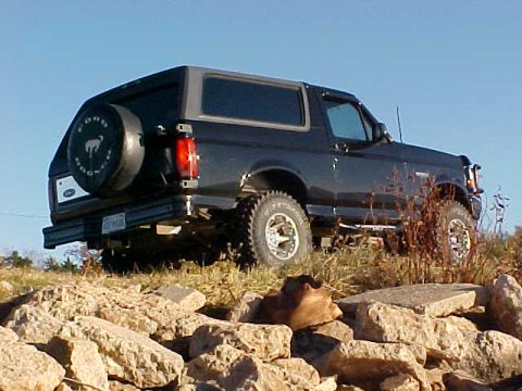 1995 Ford Bronco - This 1995 Ford Bronco is shown from the rear quarter angle, parked on a rocky terrain under a clear blue sky.