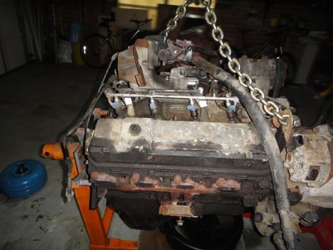 1994 Ford Bronco - Engine assembly being worked on, possibly a Ford Bronco 460, is hoisted by chains in a garage.