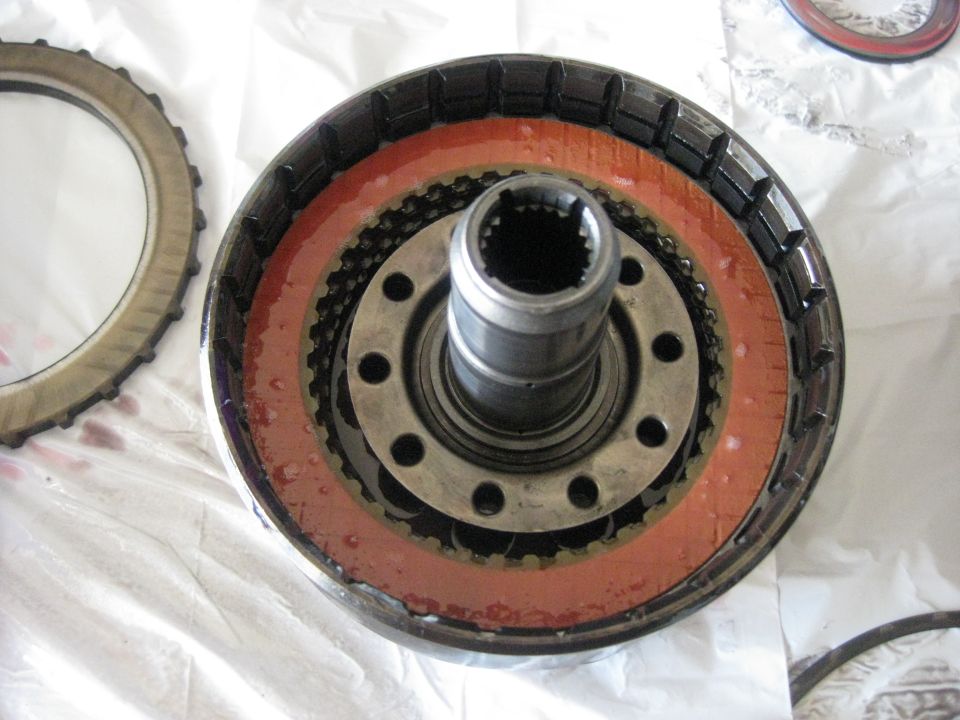 New clutches going in. You can see a friction disk here.The disks are installed in an alternating order; steel>friction>steel ect. The clutch disks should always be installed wet, especially the frictions. I have a old ATF bottle with the side cut out that I use to dip the parts in ATF before assembly.