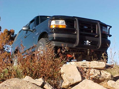1995 Ford Bronco - Black 1995 Ford Bronco navigating rocky terrain under a clear blue sky.
