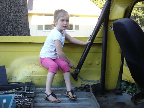 1978 Ford Bronco - Young girl sits in the bed of a yellow truck, holding onto a roll bar.