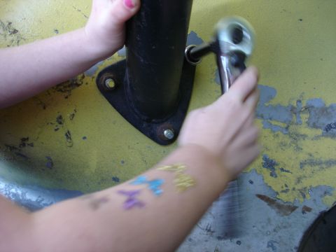 1978 Ford Bronco - A person is using a socket wrench on a bolt securing a black post to a yellow surface.