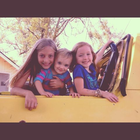 1978 Ford Bronco - Three children pose for a photo inside a yellow vehicle, with trees and a house in the background.