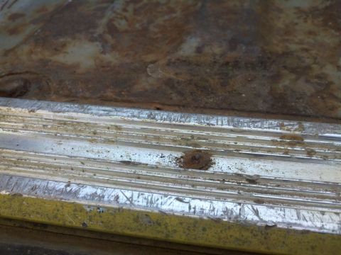 1978 Ford Bronco - Close-up of heavily rusted metal trim with horizontal grooves, showing signs of wear and tear.