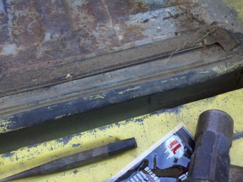 1978 Ford Bronco - Close-up of a heavily rusted panel with tools, including a chisel, hammer, and a package of disposable gloves.
