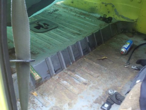 1978 Ford Bronco - The interior floor of a yellow vehicle shows signs of rust and wear, with a can of spray paint visible.
