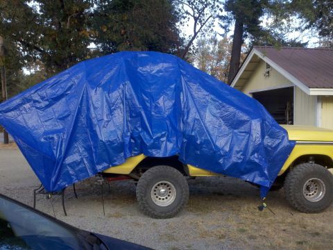 1978 Ford Bronco - A yellow 1978 Ford Bronco is partially covered by a blue tarp in front of a garage.