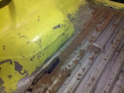 1978 Ford Bronco - A wire brush rests on the rusted floor of a yellow vehicle's interior.