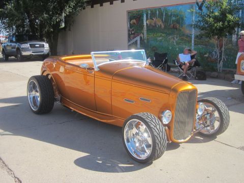 1991 Ford LTD Crown Victoria - A bright orange hot rod convertible is parked at an outdoor car show, with a pickup truck visible in the background.