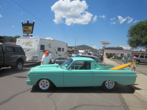 1991 Ford LTD Crown Victoria - Teal 1960 Ford Falcon Ranchero with a surfboard in the bed is parked on a street next to a trailer.