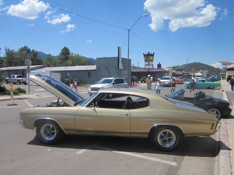 Gold 1970s Chevrolet Chevelle SS coupe with hood open, parked on street next to other cars