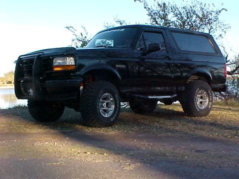 1995 Ford Bronco - This 1995 Ford Bronco is shown from the front-three-quarter view, parked outdoors with trees in the background.