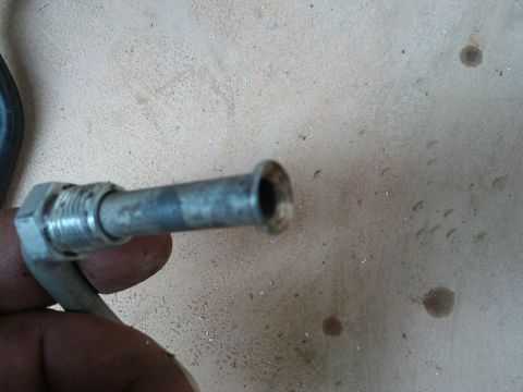 1998 Ford Crown Victoria - A metal tube fitting is held by fingers against a textured surface.