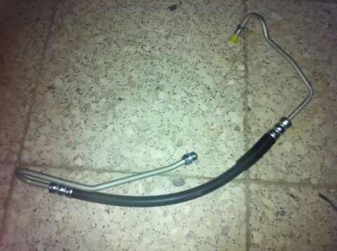 1998 Ford Crown Victoria - A power steering hose lies on a tiled floor, showing its metal and rubber components.
