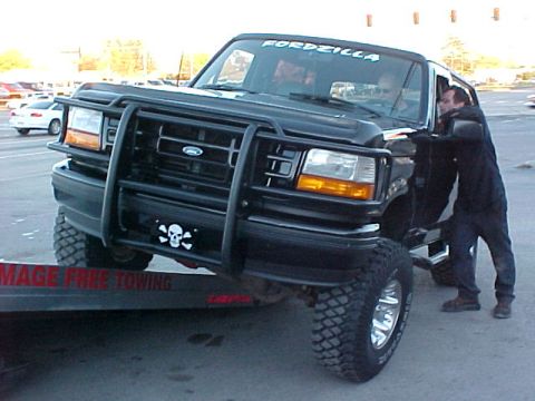 1995 Ford Bronco - A man loads a modified Ford Bronco onto a tow truck, which has "DAMAGE FREE TOWING" written on its side.