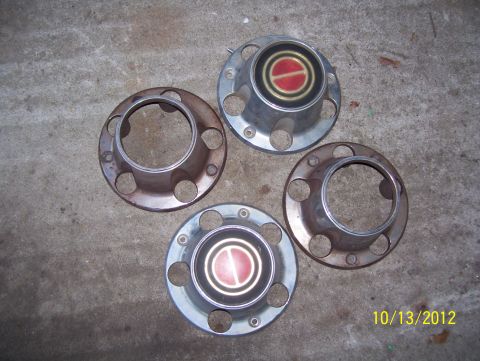 1990 Ford Bronco - A collection of four hubcaps, two of which feature a red and gold emblem, are displayed on a concrete floor.