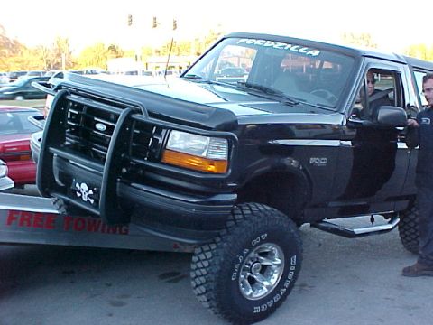 1995 Ford Bronco - A black Ford Bronco is loaded onto a trailer, displaying a "FORDZILLA" decal and a skull emblem.