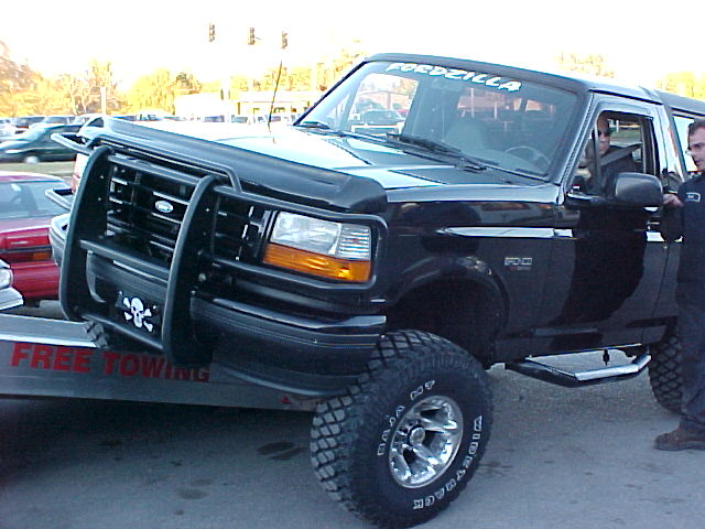Black lifted Ford Bronco on a Free Towing flatbed with men at the driver door