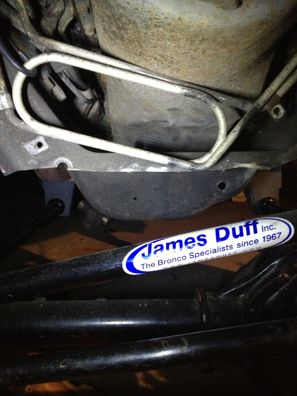 Underbody of a vehicle showing suspension components and brake lines, with a James Duff Inc. sticker