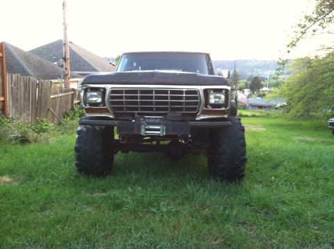 1978 Ford Bronco - This lifted 1978 Ford Bronco is parked on grass in front of a wooden fence and houses.