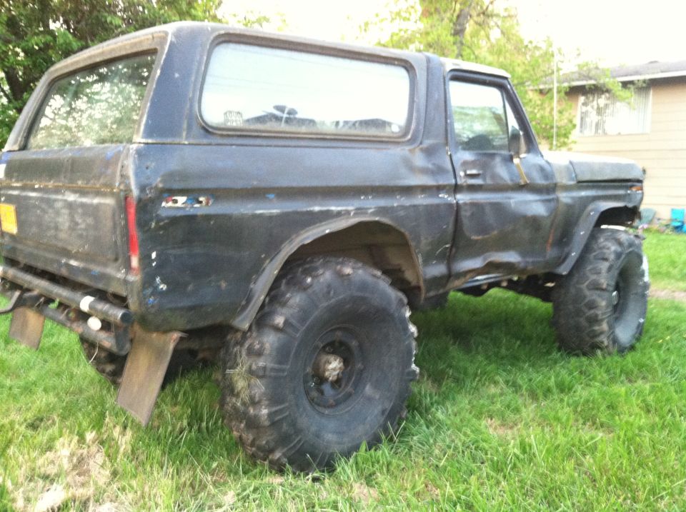 Primer-black late-70s Ford Bronco on big mud tires parked on backyard grass