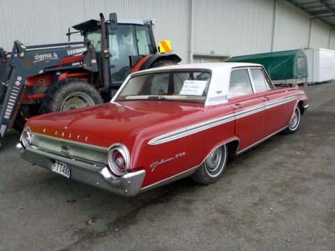 1969 Lincoln Continental - 1962 Ford Galaxie 500 sedan, red with white roof, parked outdoors near a tractor and trailers.