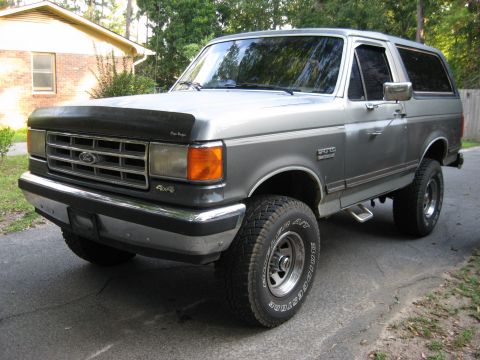 1988 Ford Bronco - This two-tone Ford Bronco is shown from a three-quarter front angle, parked in front of a house.