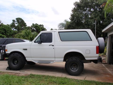 1995 Ford Bronco - A white Ford Bronco is parked in a driveway with a lifted suspension and large off-road tires.