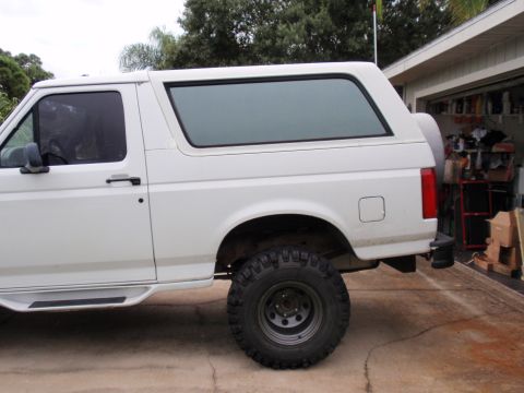 1995 Ford Bronco - This white Ford Bronco, likely from the early to mid-1990s, is shown from the side with a lifted suspension and off-road tires.
