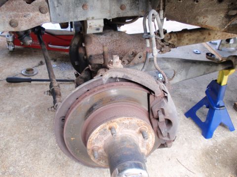 1995 Ford Bronco - Close-up view of the front wheel brake assembly and suspension components, with the vehicle supported by jack stands.