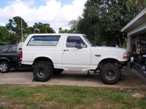 1995 Ford Bronco - A lifted 1995 Ford Bronco is parked outside a garage, with another vehicle visible to its left.