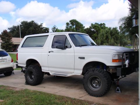 1995 Ford Bronco - A white 1995 Ford Bronco is shown with a lifted suspension and oversized tires, parked in front of a house.