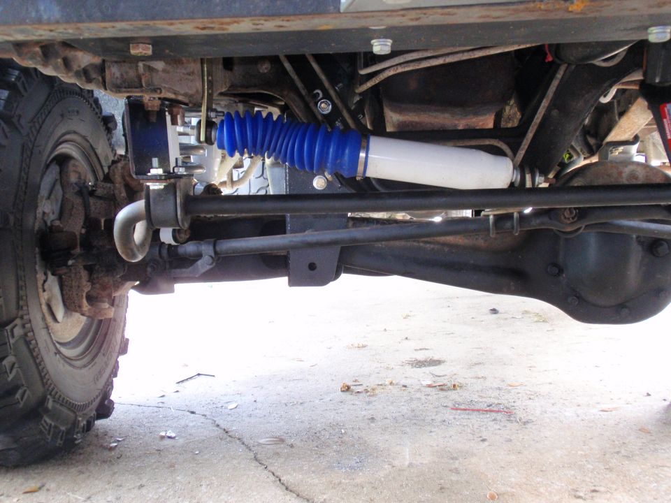 Close-up of vehicle's front axle, steering linkage, and shock absorber with blue bellows