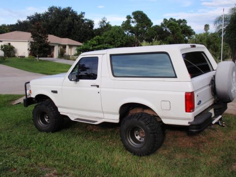 1995 Ford Bronco - A white Ford Bronco is parked on a grassy lawn in front of a suburban house.