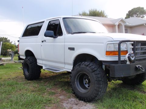1995 Ford Bronco - White 1995 Ford Bronco with off-road tires and aftermarket bumper parked on grass.