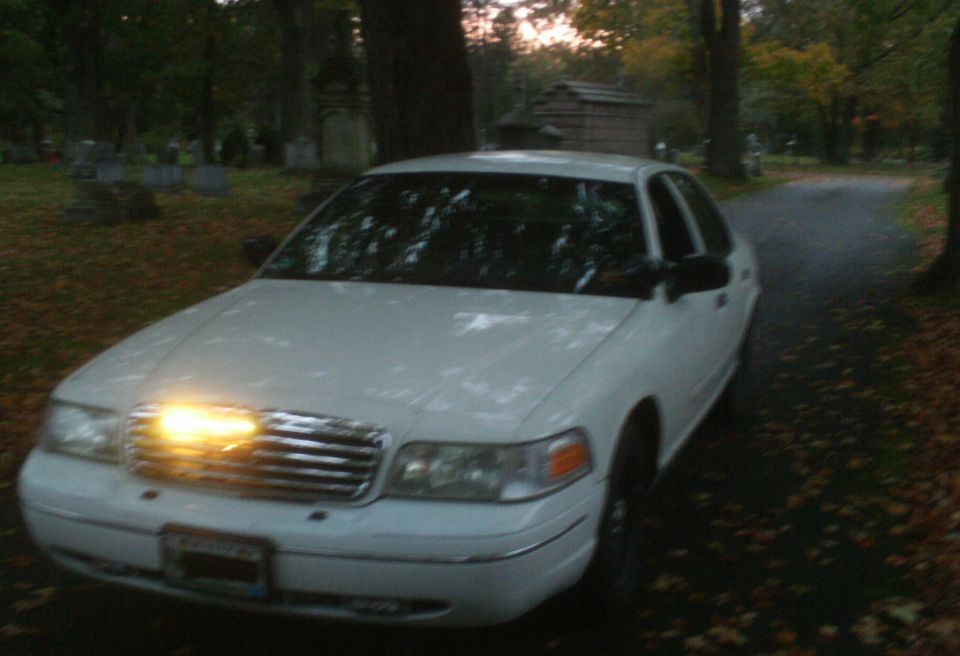 1998 Ford Crown Victoria parked on a leaf-covered road in a cemetery during twilight