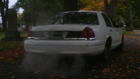 1998 Ford Crown Victoria - A white sedan emits smoke while parked in a cemetery during autumn.