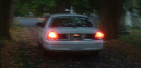 1998 Ford Crown Victoria - A white 1998 Ford Crown Victoria is viewed from the rear, its brake lights illuminated, in a dimly lit outdoor setting.
