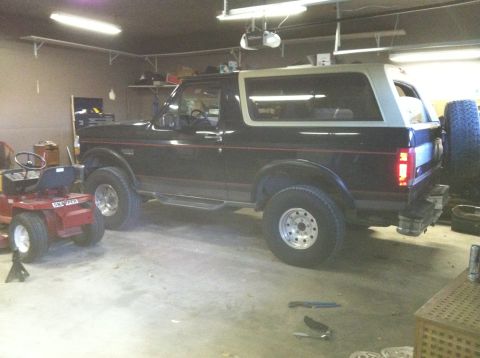 1994 Ford Bronco - A black Ford Bronco and a red riding mower are parked inside a garage.