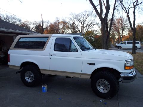 1996 Ford Bronco - Side view of a white 1996 Ford Bronco with tan accents and a tan removable roof, parked in a driveway.