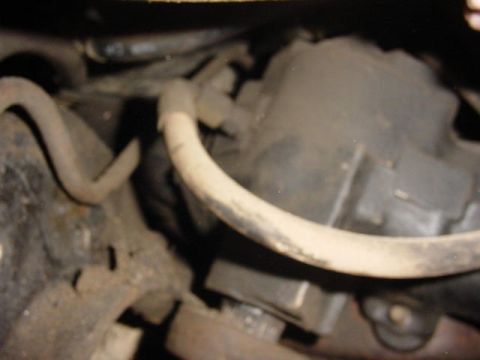 1992 Ford Bronco - Blurry close-up of dirty undercarriage or engine-bay components, with a grime-coated curved hose or bar crossing in front of a dark cast ho…