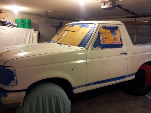 1996 Ford Bronco - A white SUV is being prepped for painting, with windows taped off and blue masking tape along the lower body.