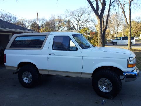 1996 Ford Bronco - A white Ford Bronco with a tan removable top is parked in a driveway, with a white van visible on the street.
